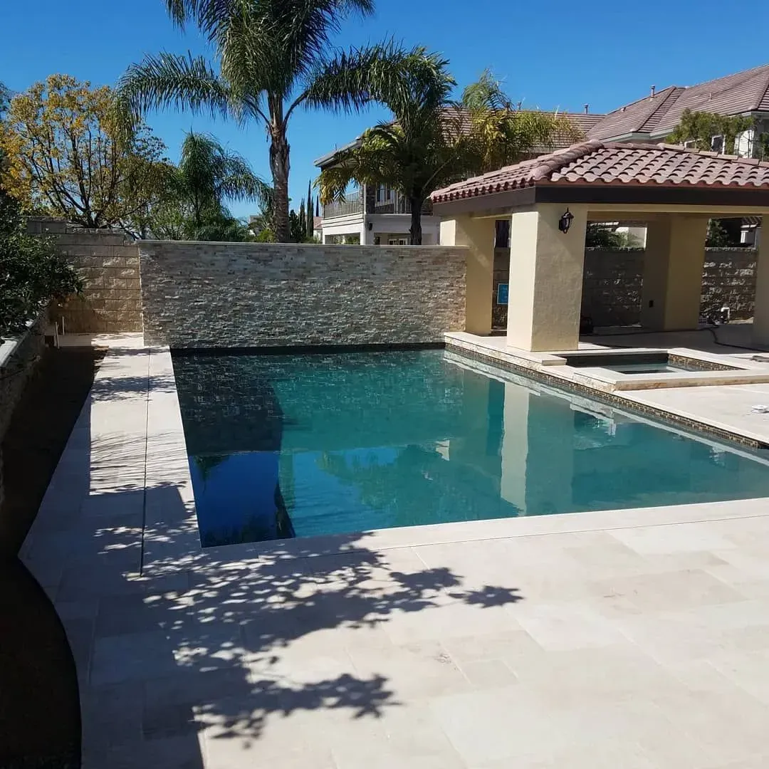 Swimming pool with stone wall and cabana on sunny day.