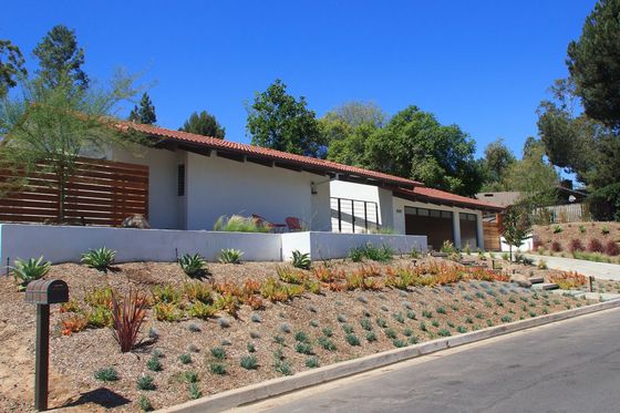 Pool construction site with concrete basin, dirt ground, and a retaining wall in a suburban backyard.