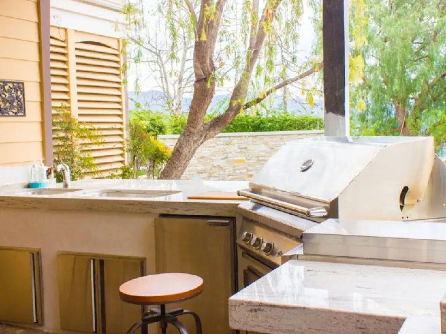 Outdoor kitchen with grill, sink, and cabinetry set against a natural, green backdrop.