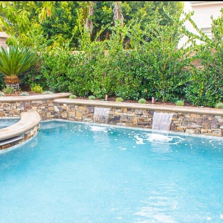 Swimming pool with waterfalls and lush green hedges.