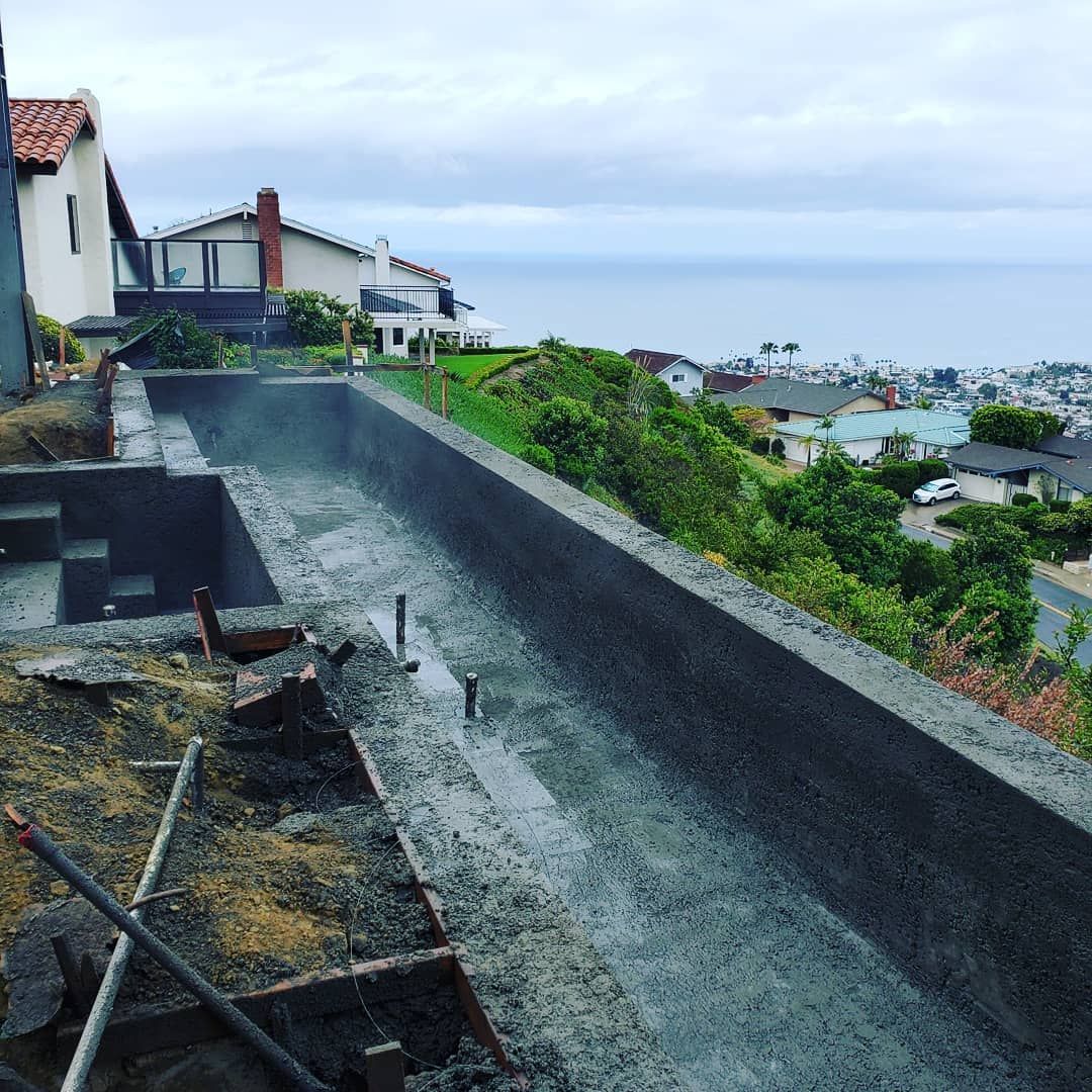 Pool construction on a hillside with ocean views, concrete structure in progress.