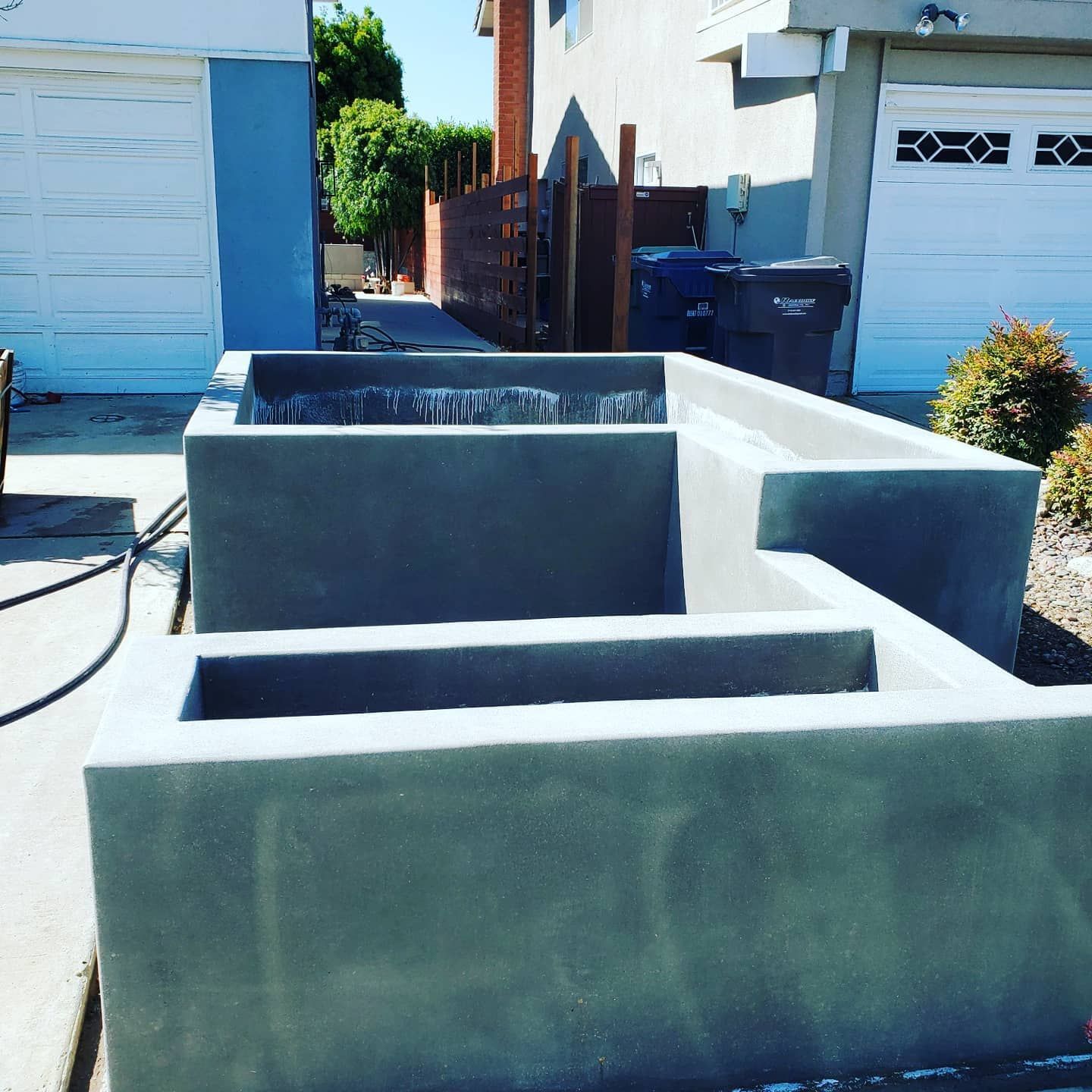 Concrete planters in front of garage doors, with trash cans and wooden fence in the background.