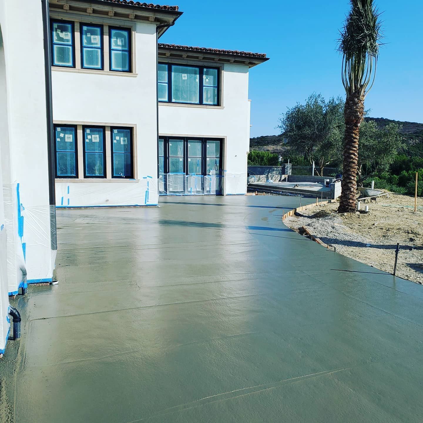 Newly poured concrete driveway in front of a white two-story house, under a clear blue sky.