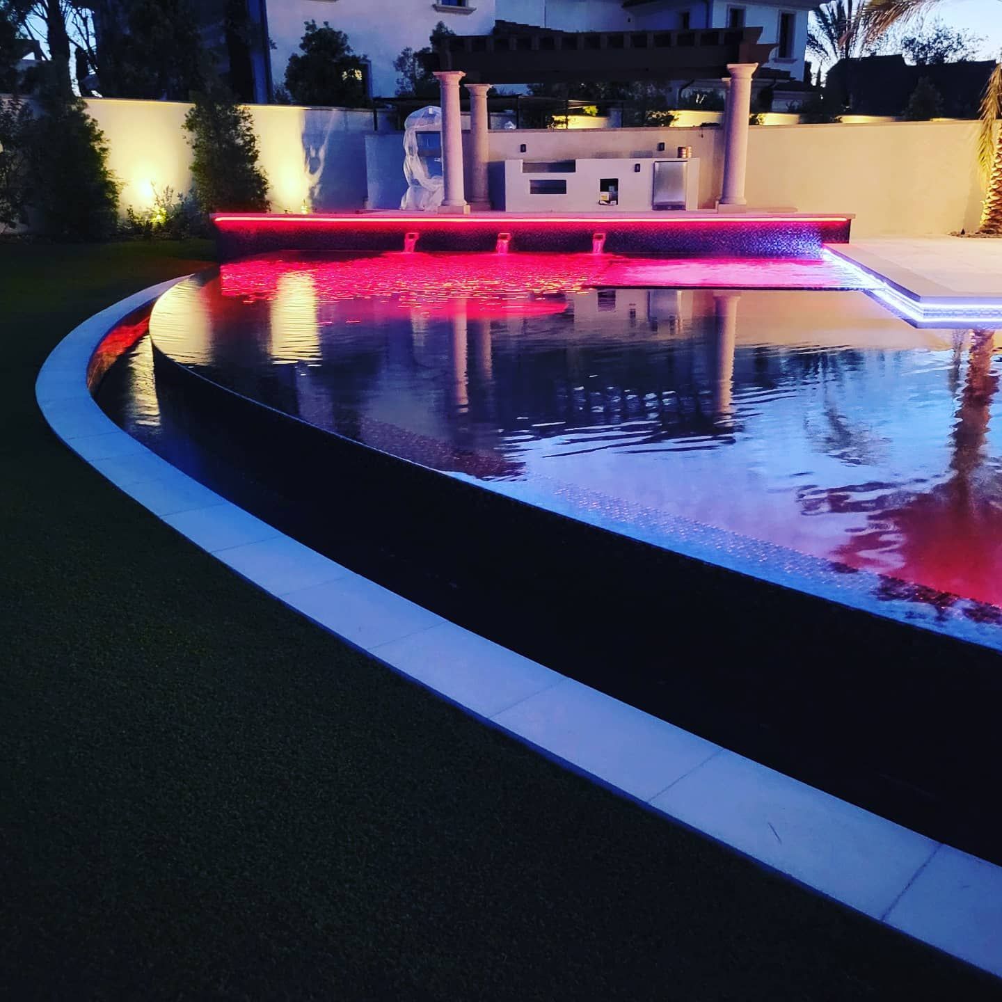 Illuminated outdoor pool with red and blue lights reflecting, night.