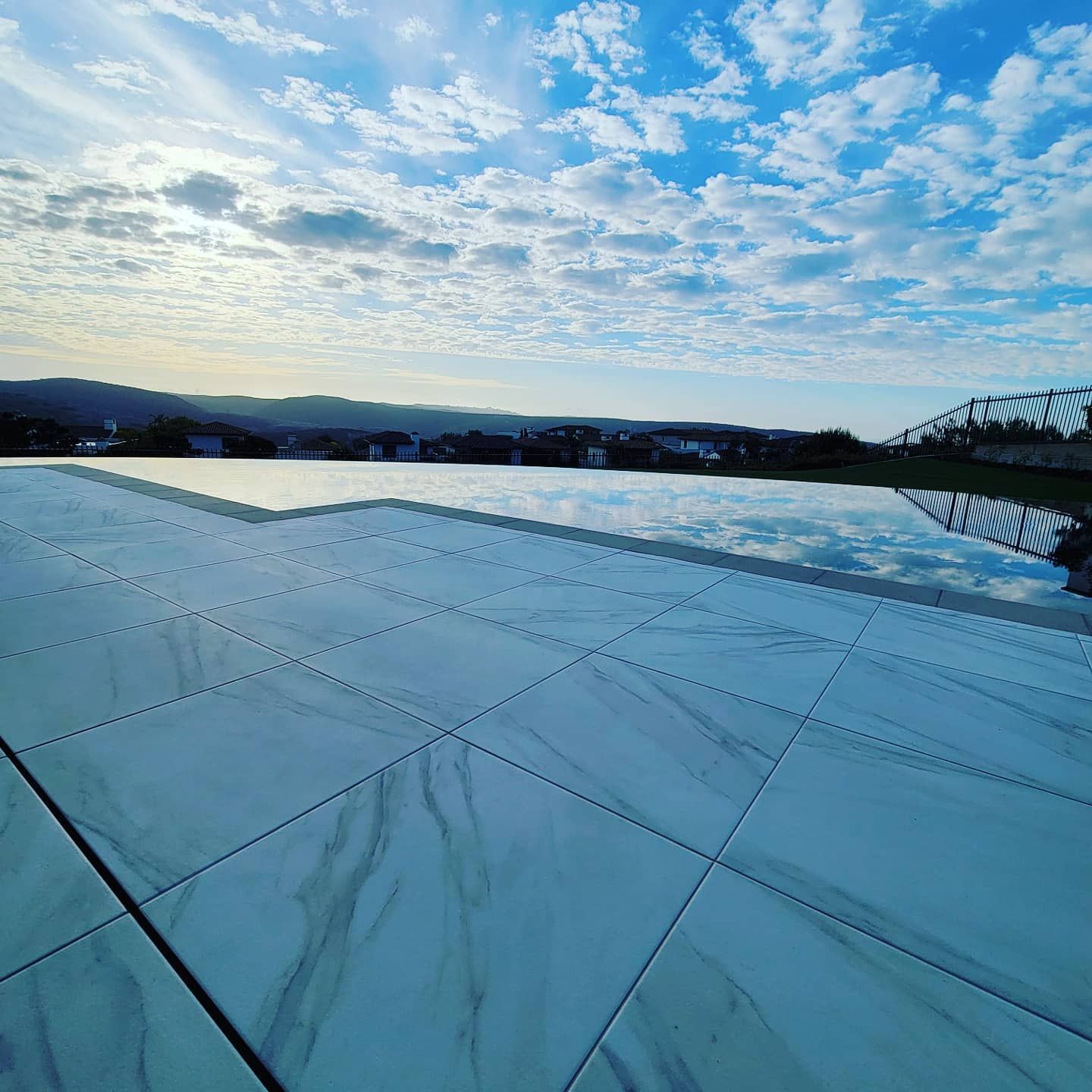 Infinity pool with a reflective surface against a cloudy blue sky. A distant town is visible.