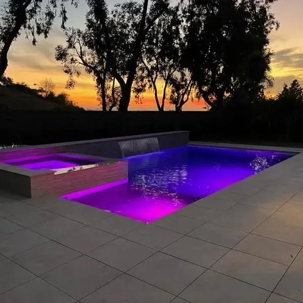A pool and jacuzzi with purple lights at sunset. Trees and a hillside in the background.