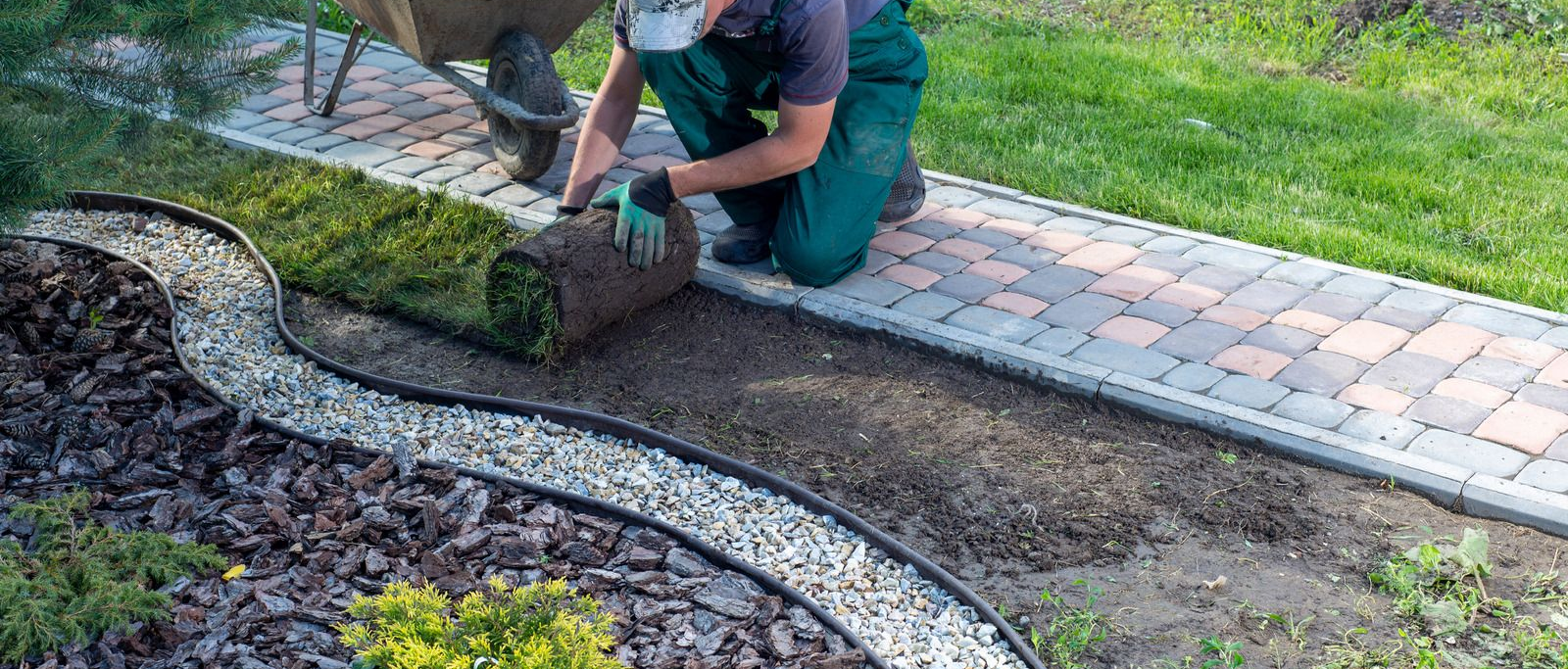 Person installing sod alongside a decorative stone border and brick pathway.