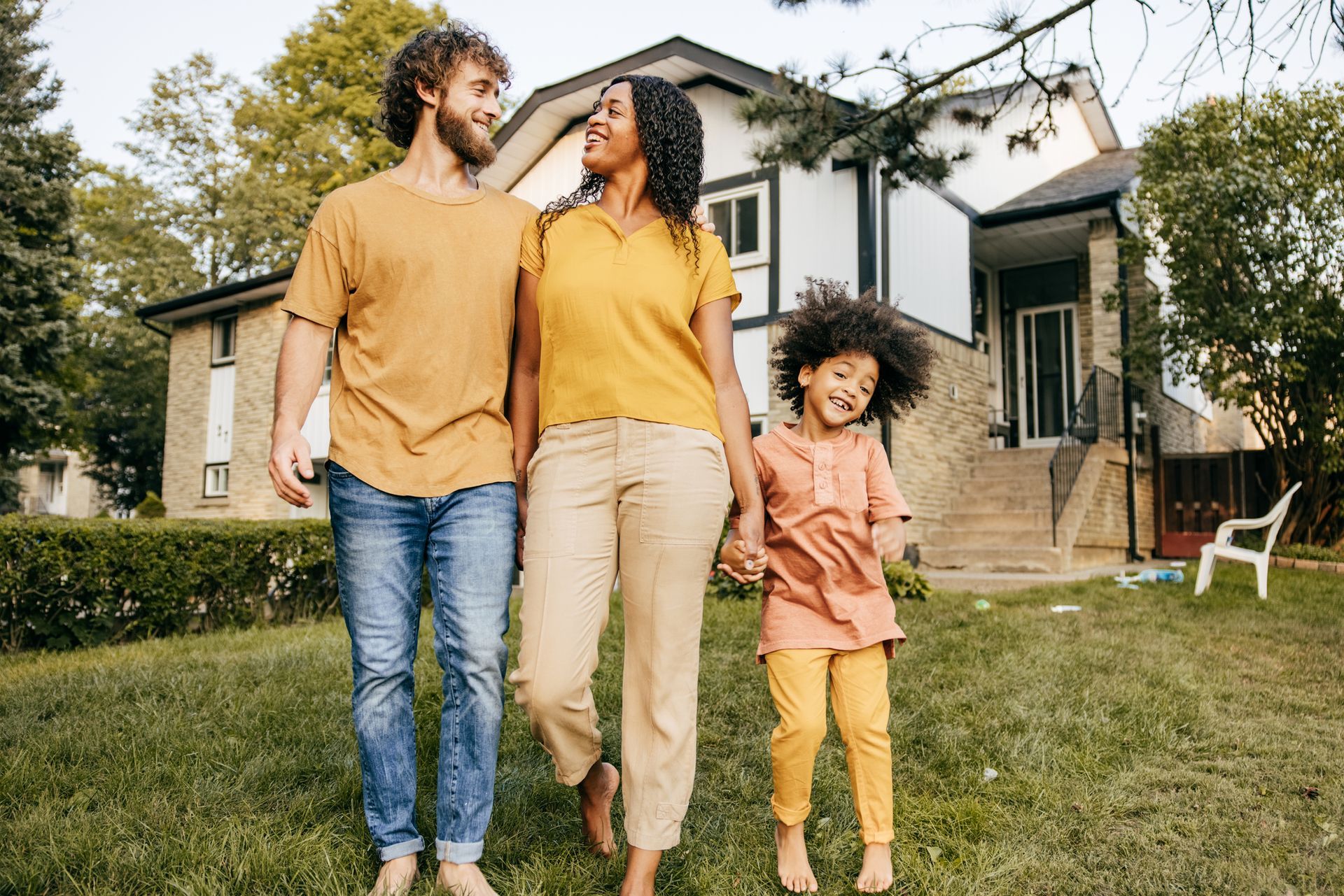 A family is walking in front of their house holding hands.