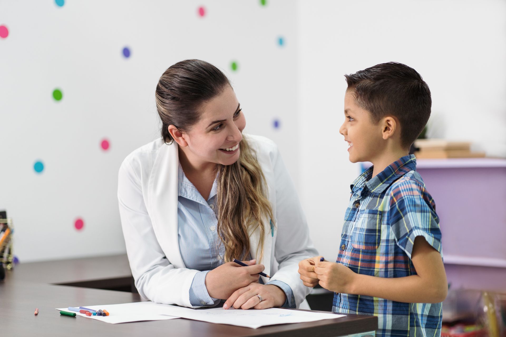 A woman is sitting at a table talking to a young boy.