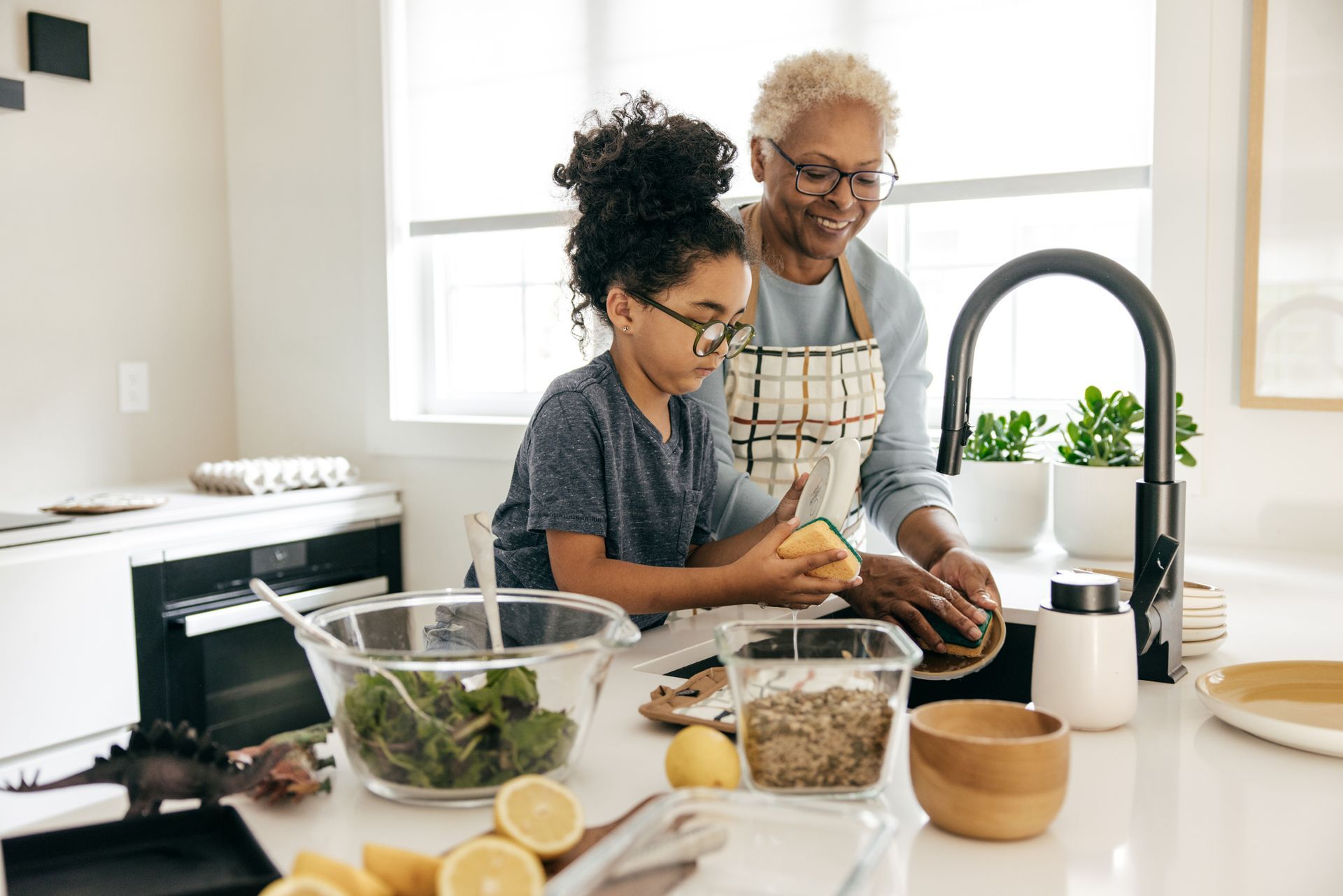 An elderly woman and a young girl are washing vegetables in a kitchen.