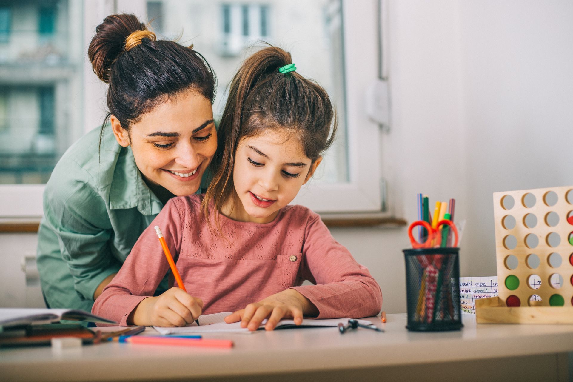 A woman is helping a little girl with her homework at a desk.