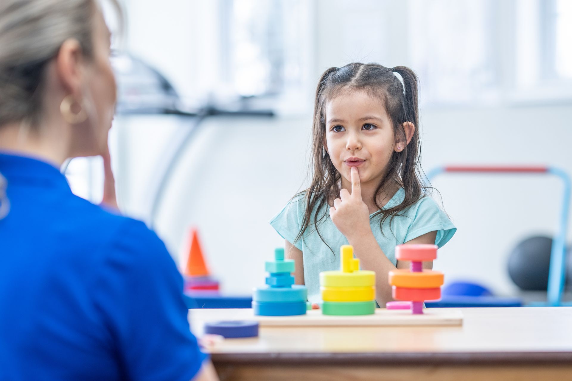 A little girl is sitting at a table playing with a stacking toy.