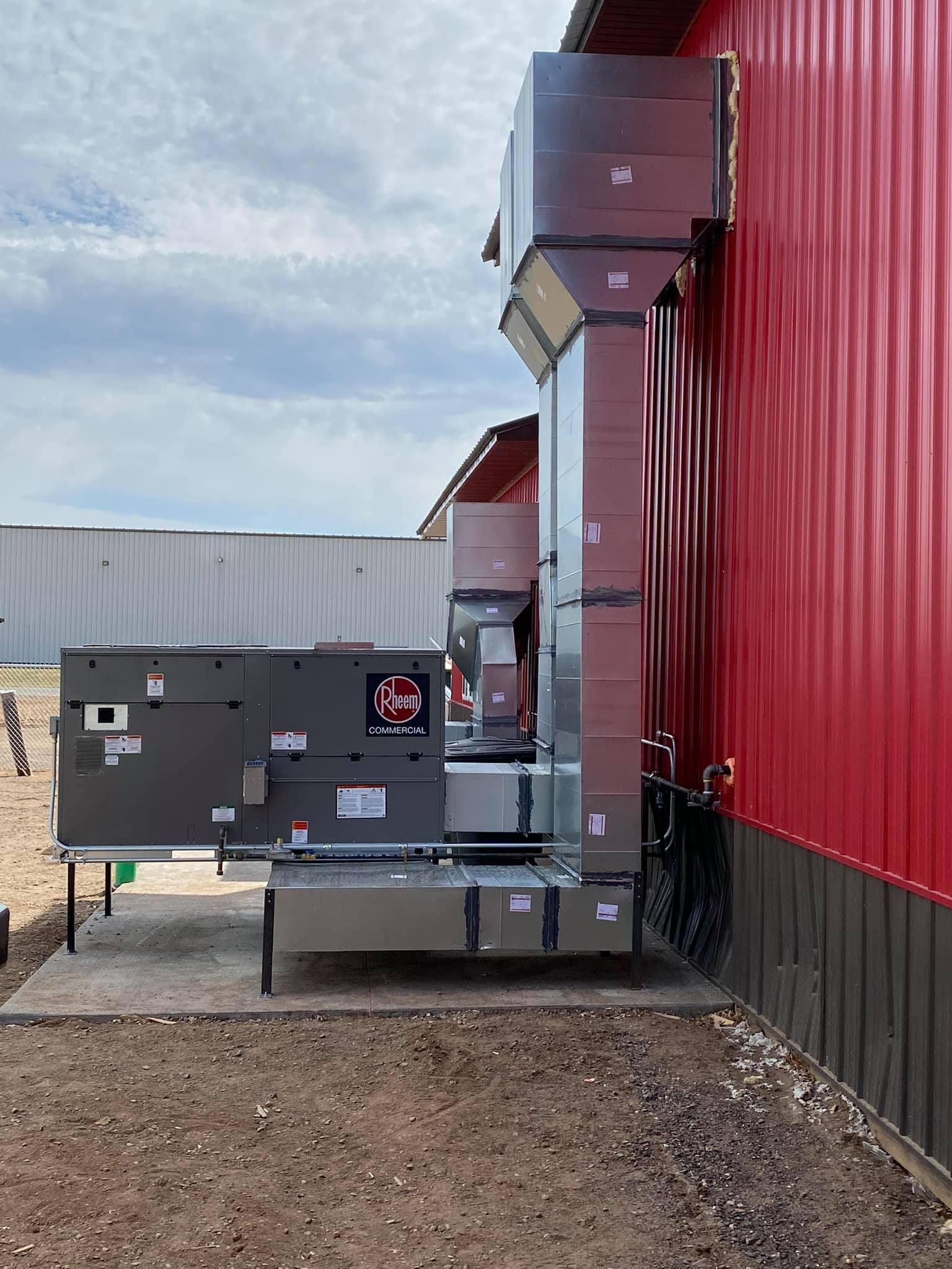 HVAC units and ductwork mounted on the side of a red building, against a cloudy sky.