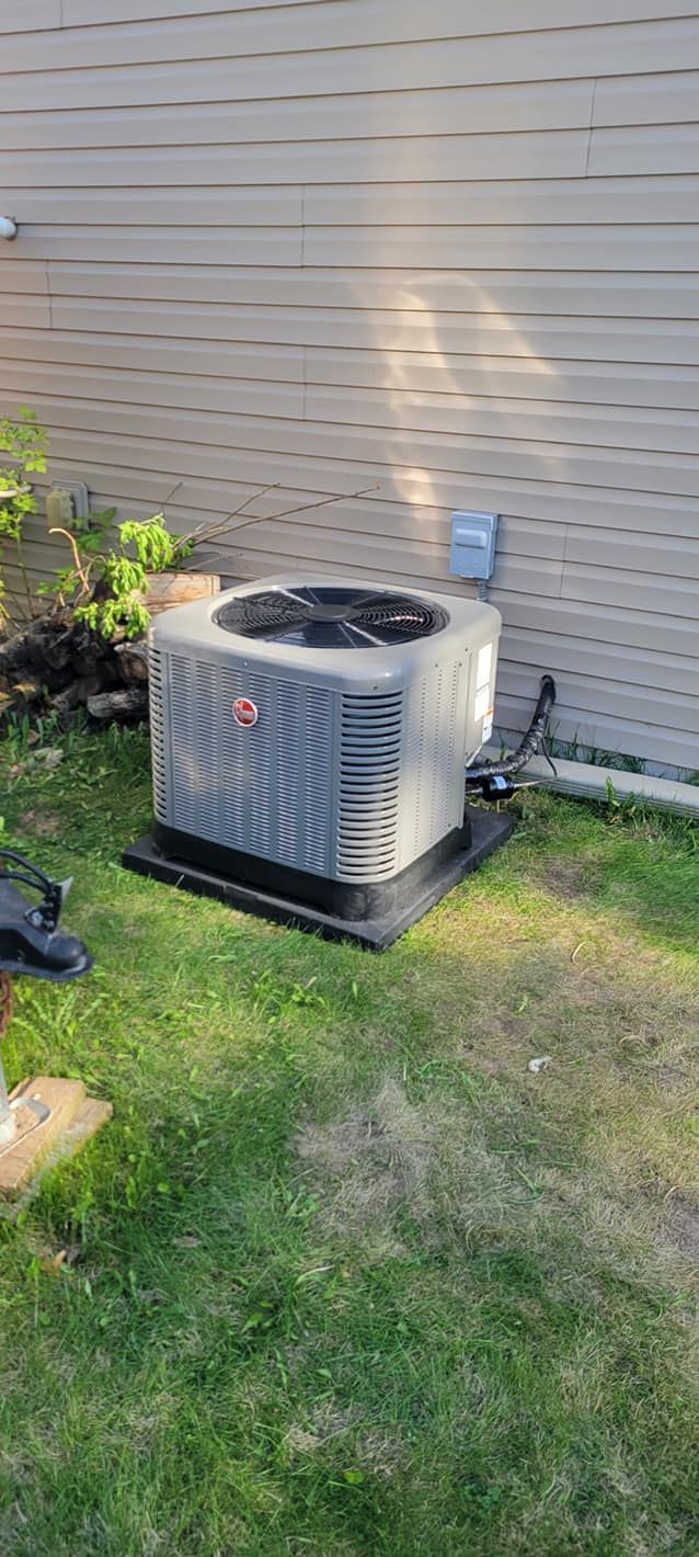 Air conditioning unit on a black base sits in a grassy yard next to a building with siding.