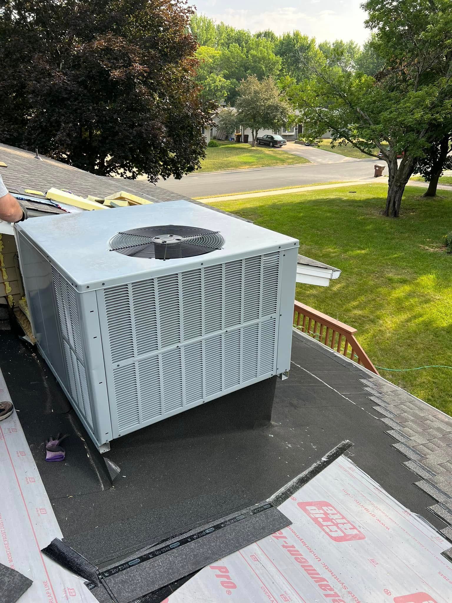 AC unit on a rooftop, surrounded by roofing materials, with a suburban street in the background.