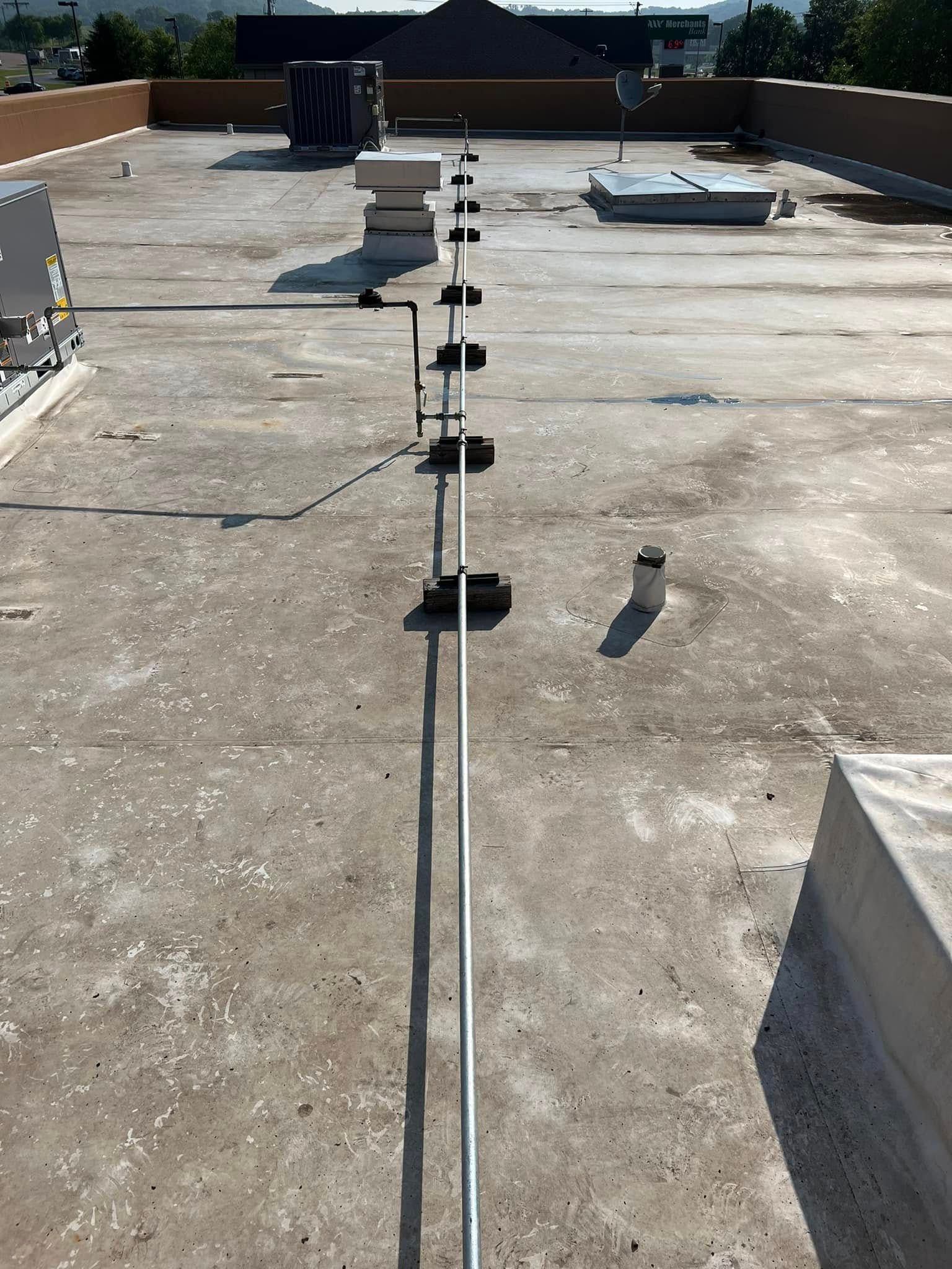Rooftop with a long, metal railing. Concrete surface with equipment and vents. Sunny day.