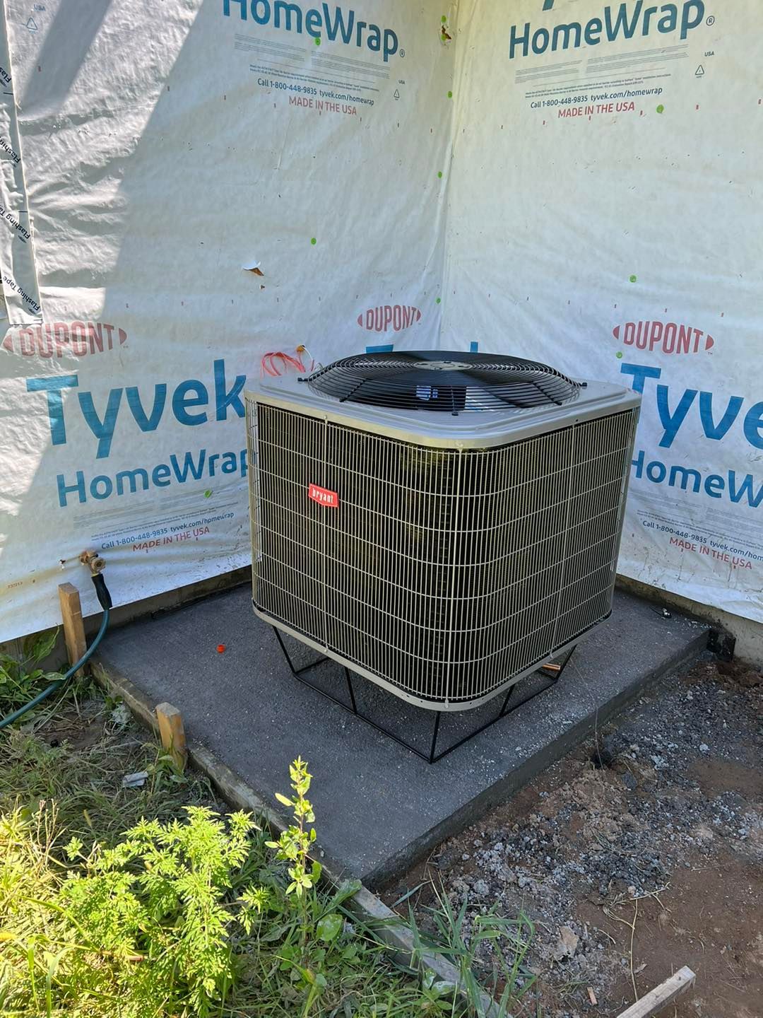 Air conditioning unit on a concrete pad, next to building wrapped in Tyvek.