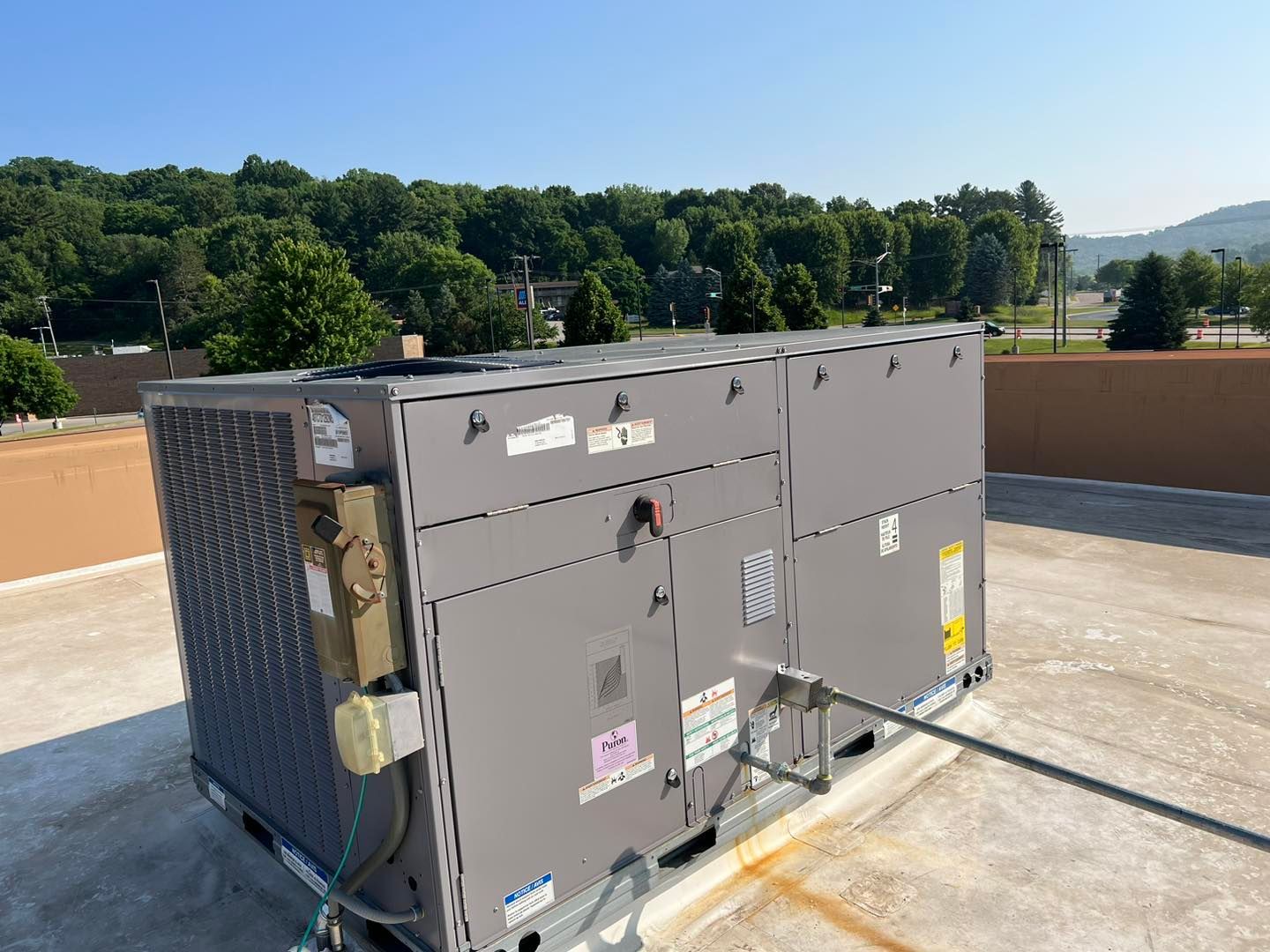 Large, gray HVAC unit on a rooftop, with a backdrop of trees and a blue sky.