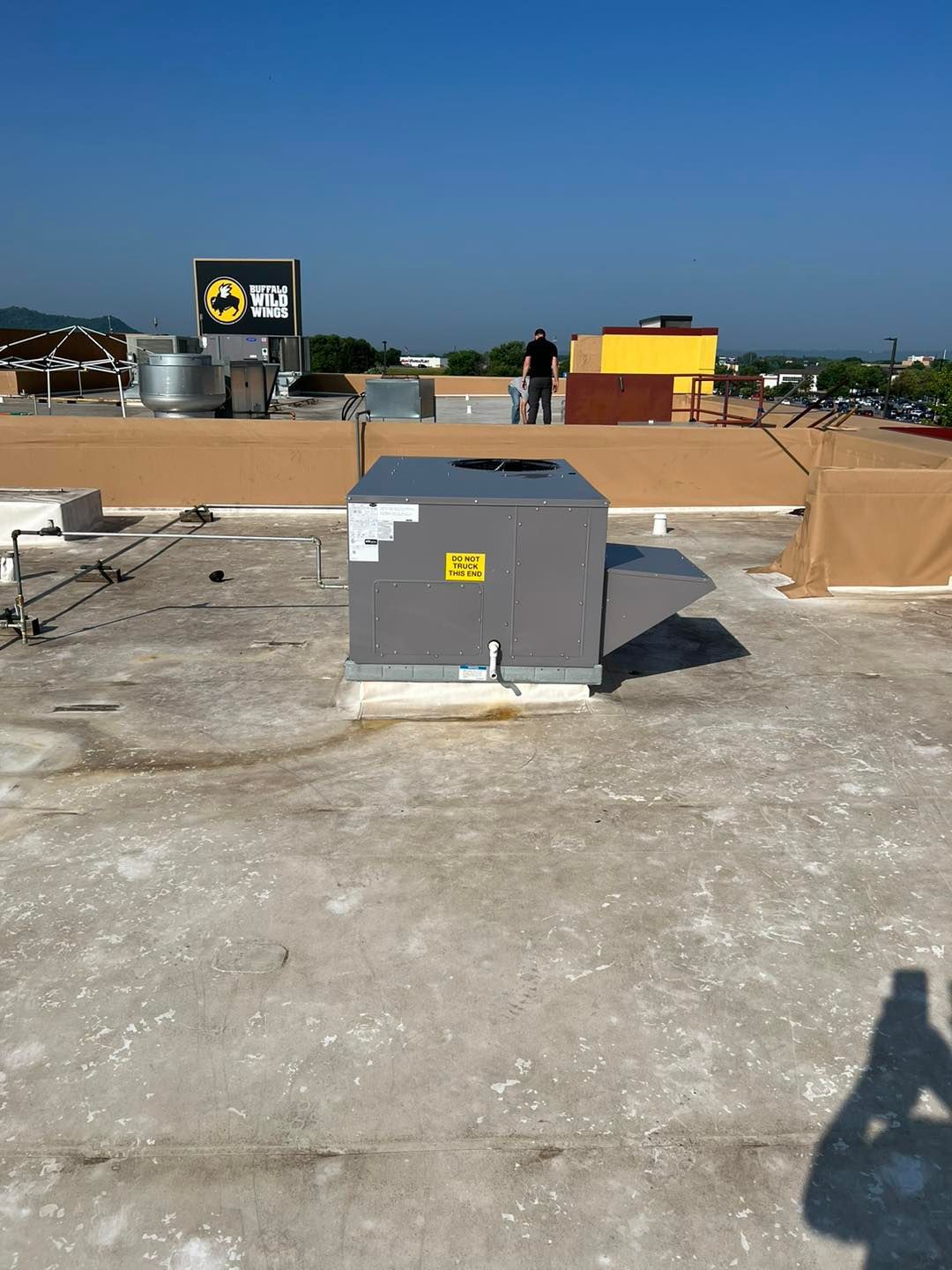 Rooftop view with HVAC unit, person standing, and signage. Sunny day with a clear blue sky.
