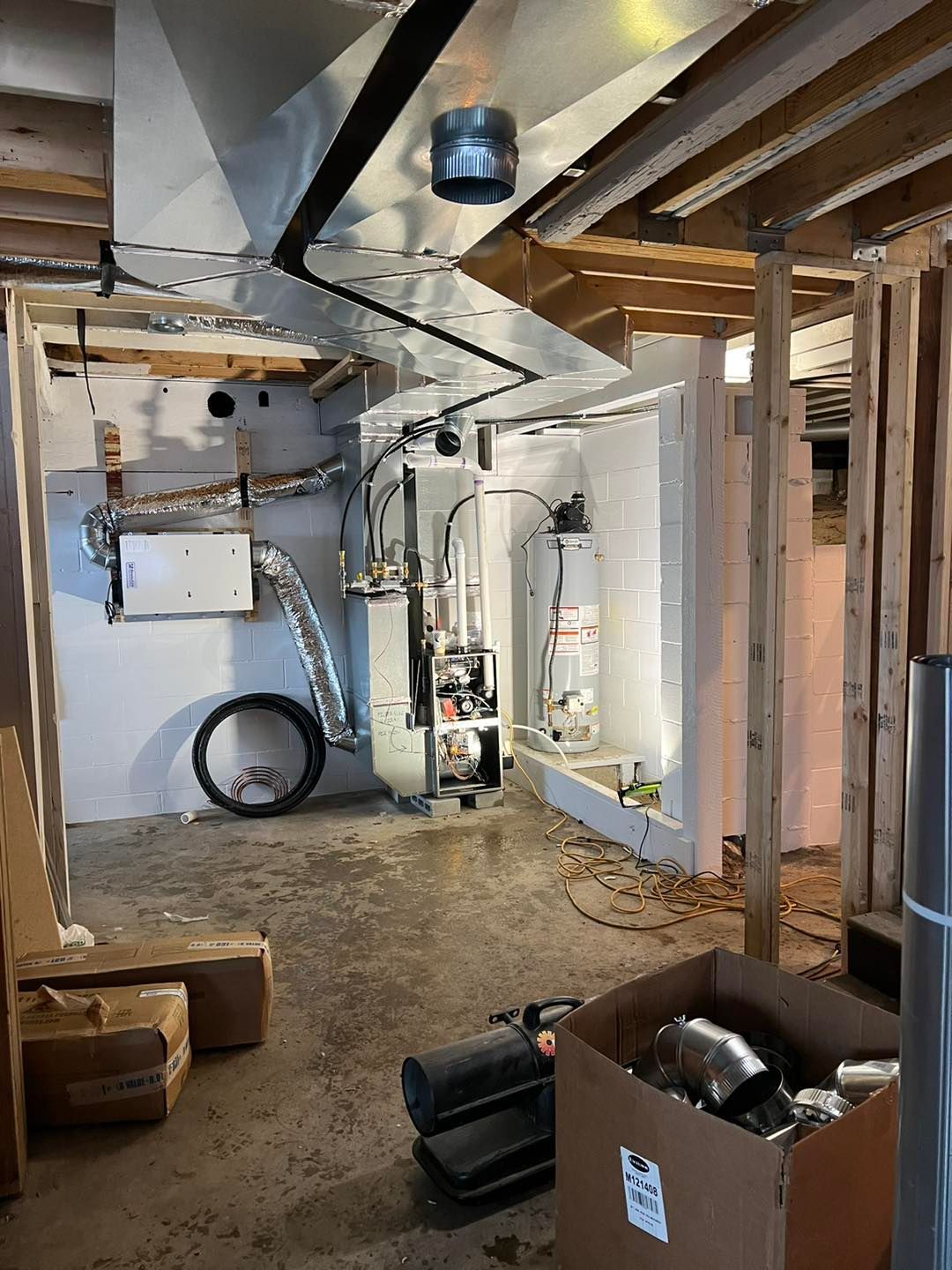 Basement with furnace and water heater. Ductwork and exposed framing. Boxes and tools on floor.