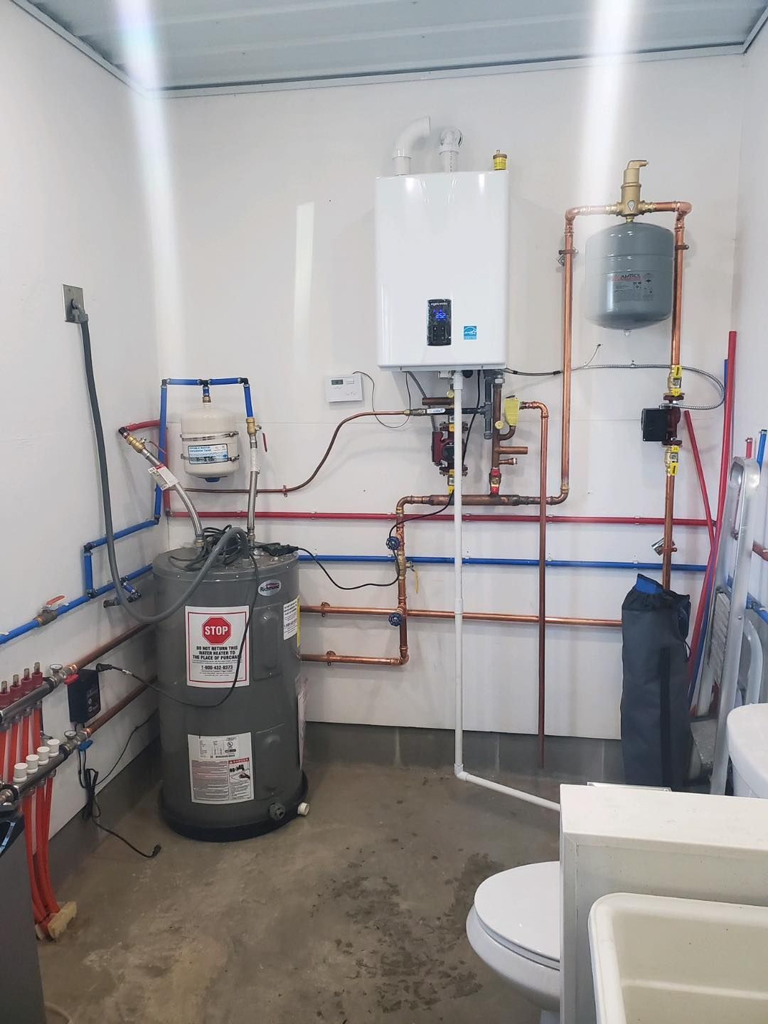 Water heater and plumbing in a utility room. Copper pipes and a white tankless water heater are visible.