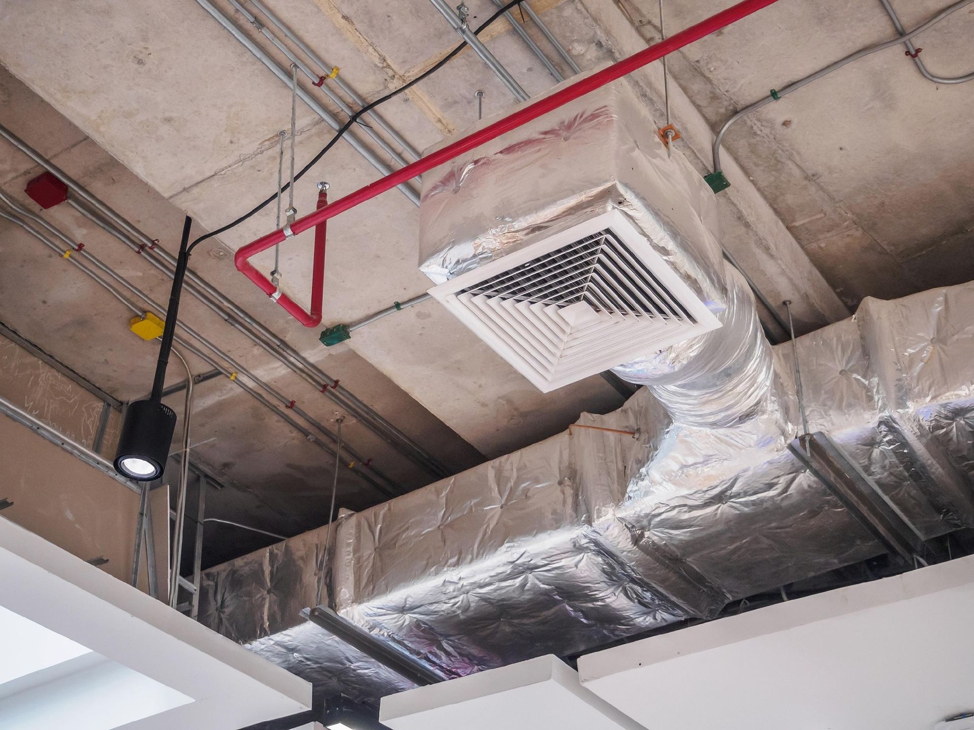 Ventilation system components exposed on a concrete ceiling, including ductwork, vents, and piping.