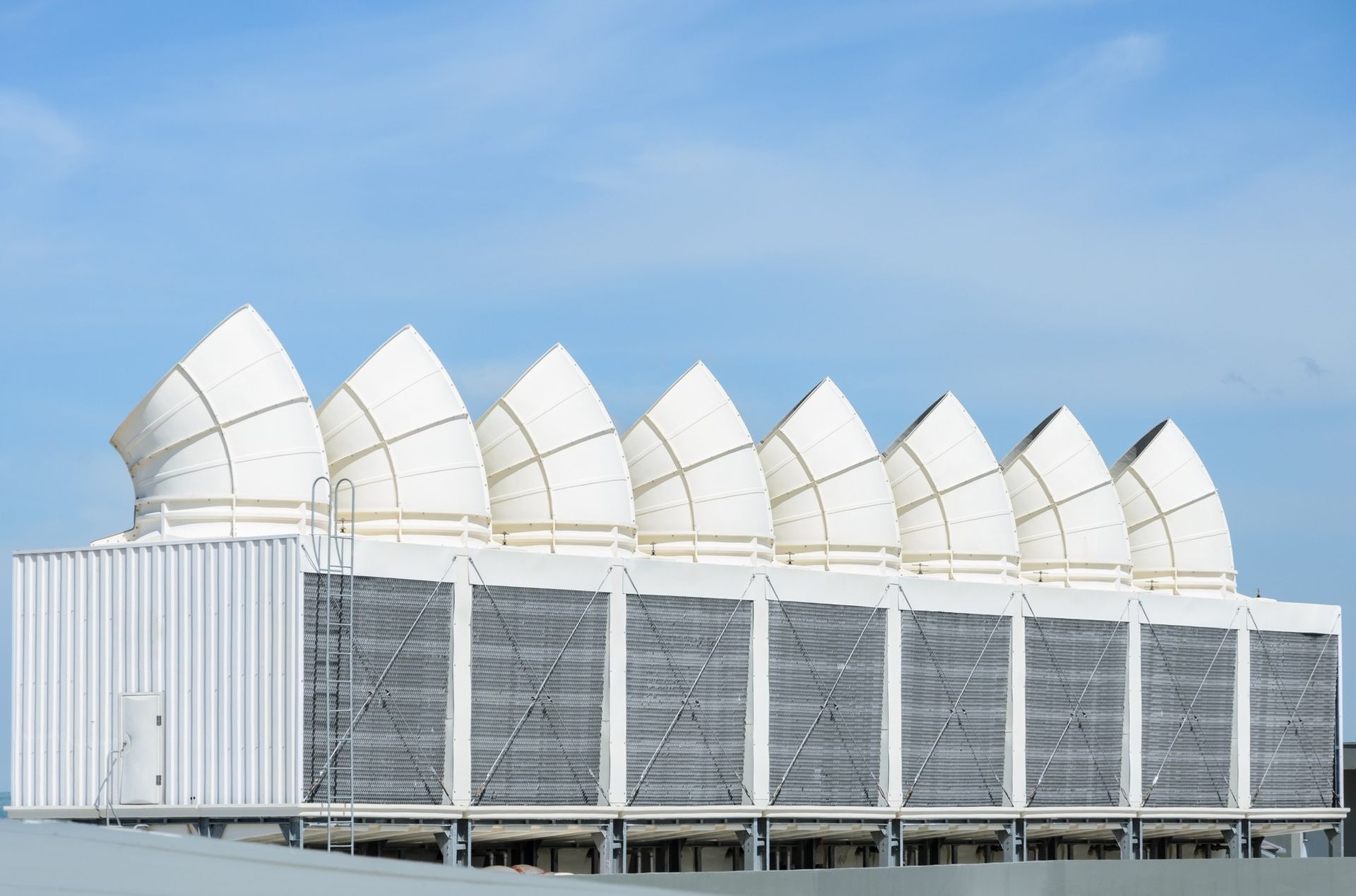 White HVAC units with conical vents on a rooftop against a blue sky.