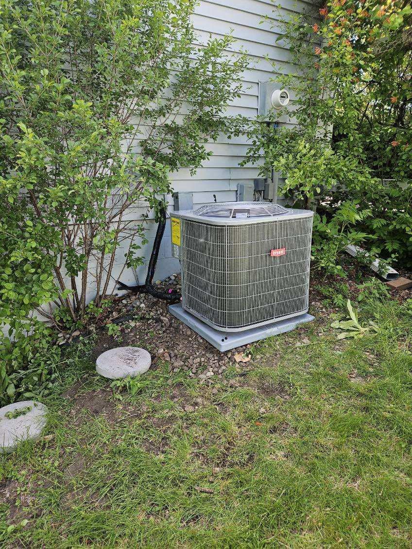 AC unit outside, surrounded by bushes and grass. White siding in the background.