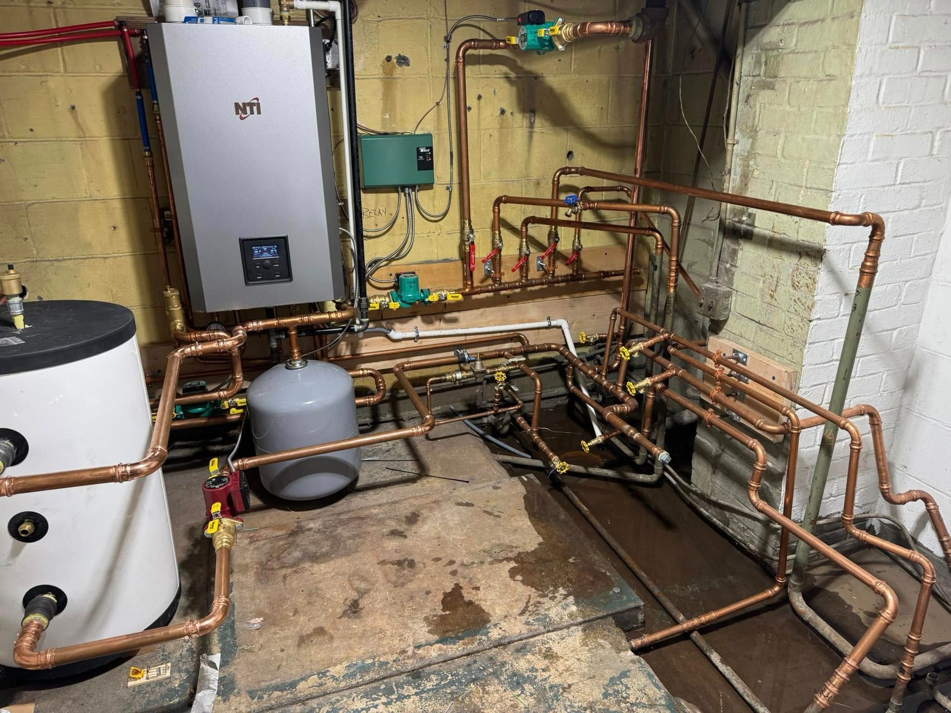 Basement with heating system components, including a boiler, water tank, and copper pipes.