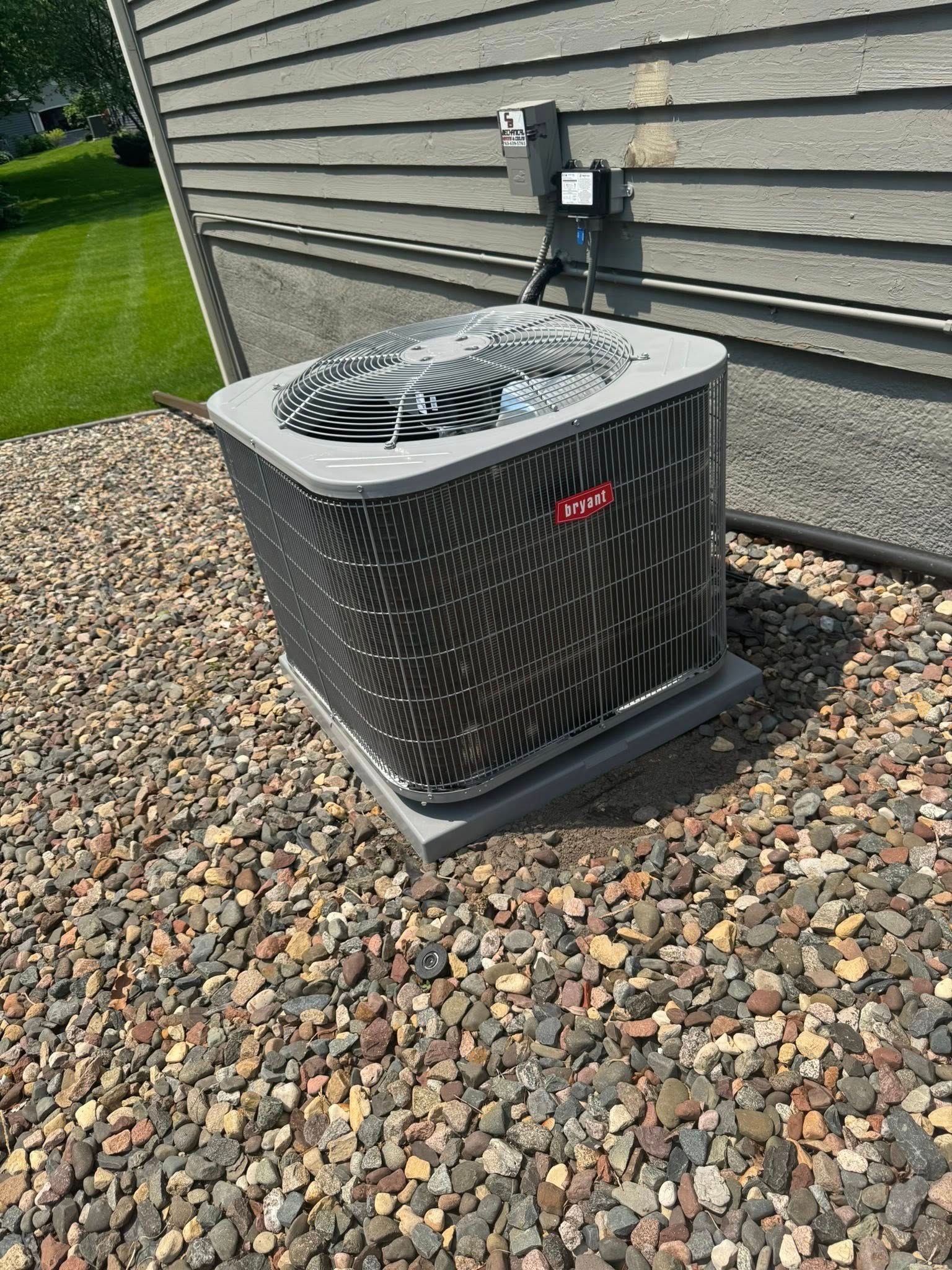 Bryant air conditioner unit on gravel near a house with gray siding.