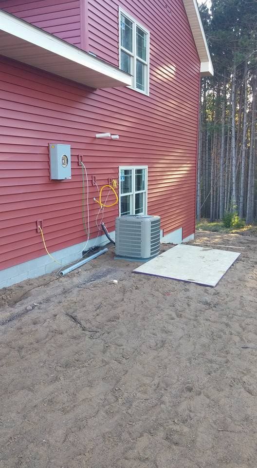 Red house exterior with air conditioning unit on a gravel surface. Electrical box on the wall.