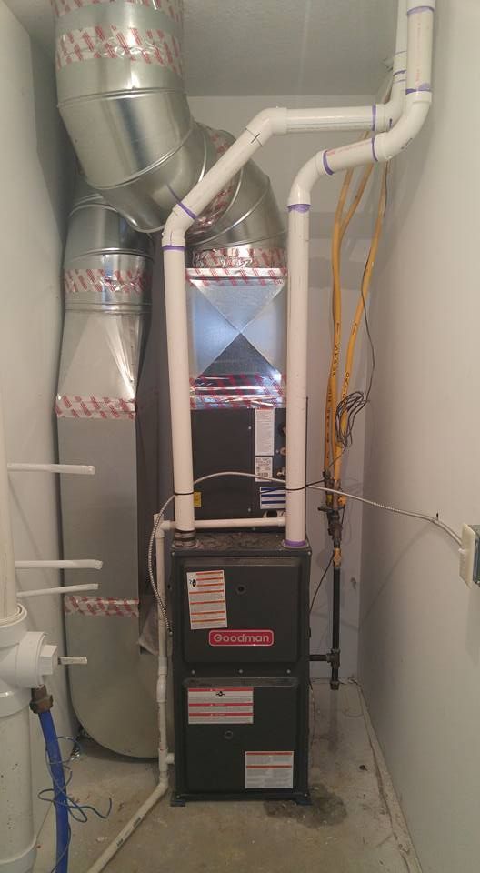 Furnace and ductwork in a utility room. Metal ducts, PVC pipes, and a black furnace unit.