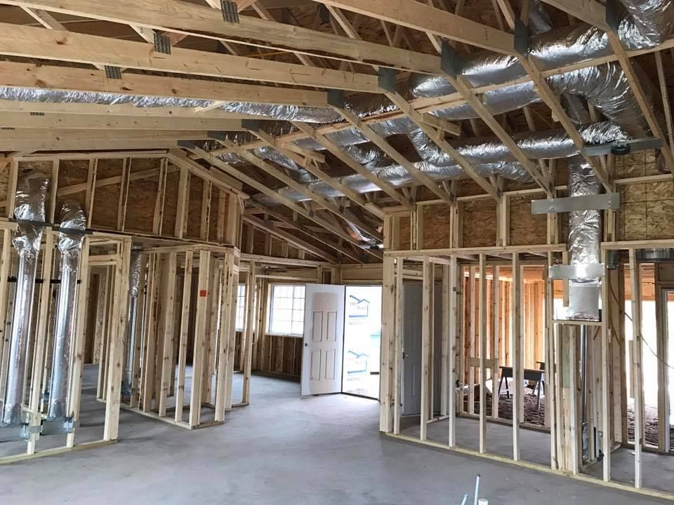 Interior view of a building under construction, showing wooden framing, ductwork, and open doorways.