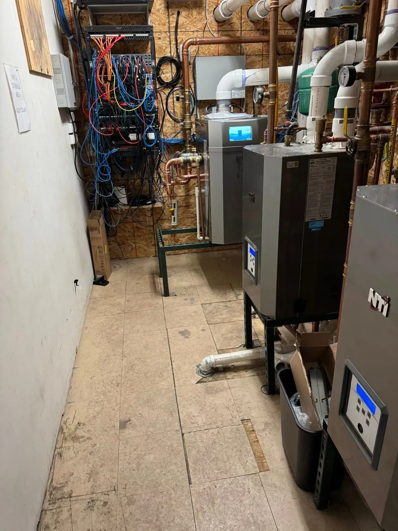 Boiler room with three gray boilers, pipes, and wiring.