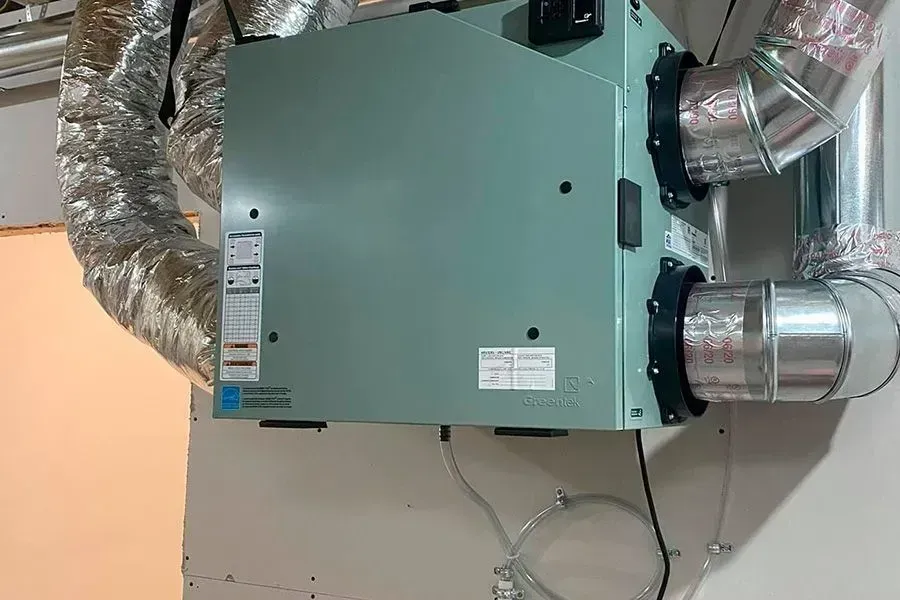 Green HVAC unit with attached ductwork against a beige wall.