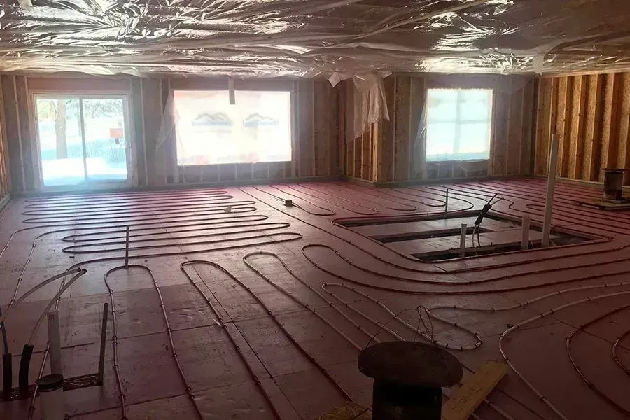 Interior room under construction, with pink insulation and radiant heating tubing installed on the floor.