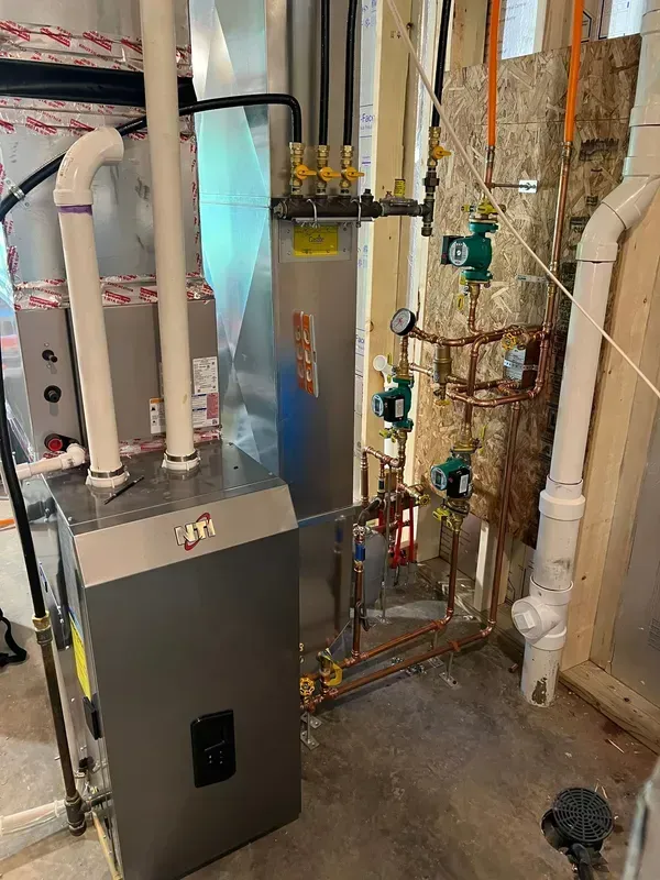 HVAC system with furnace, ductwork, pipes, and pumps in a basement setting.