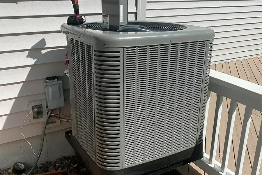 Gray air conditioner unit on a deck, with a utility box and wires visible.