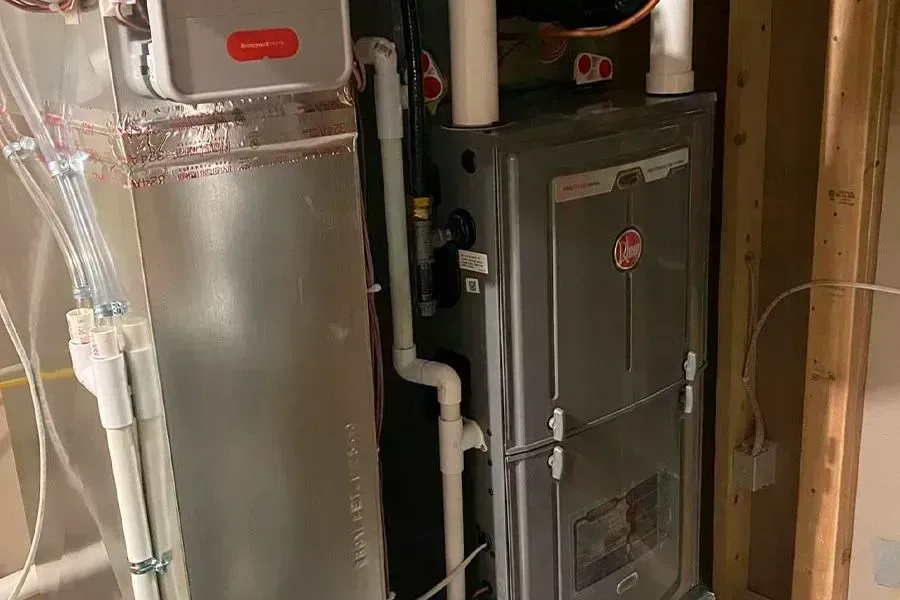 Furnace and water heater in a utility room. Gray metal units, pipes, and electrical wiring.