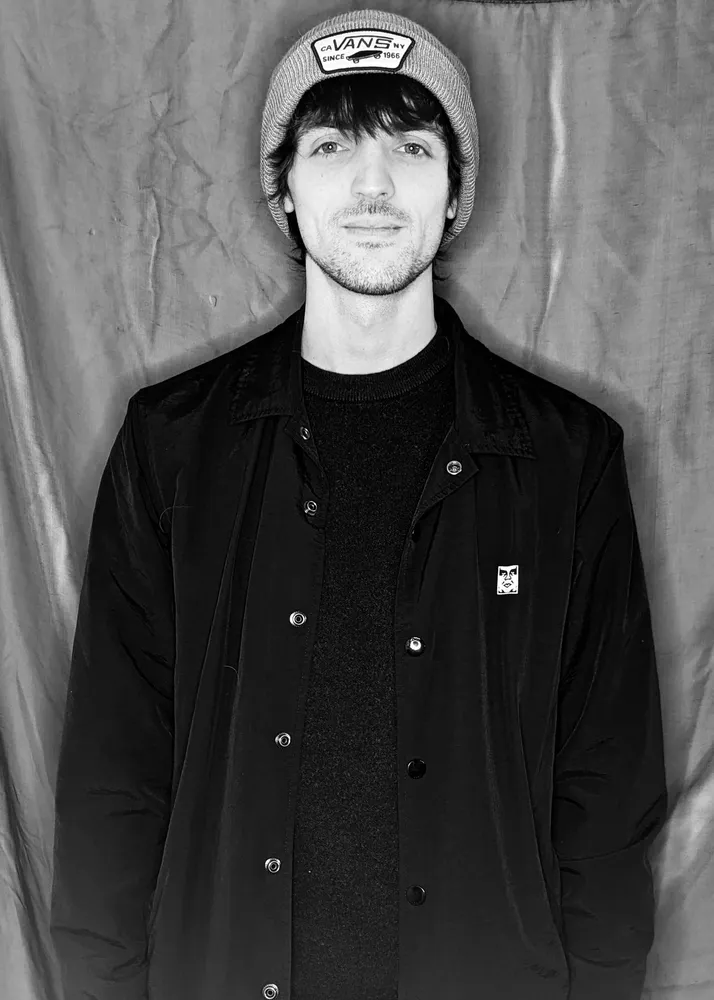 Man in beanie and jacket, looking at the camera. Black and white photo.