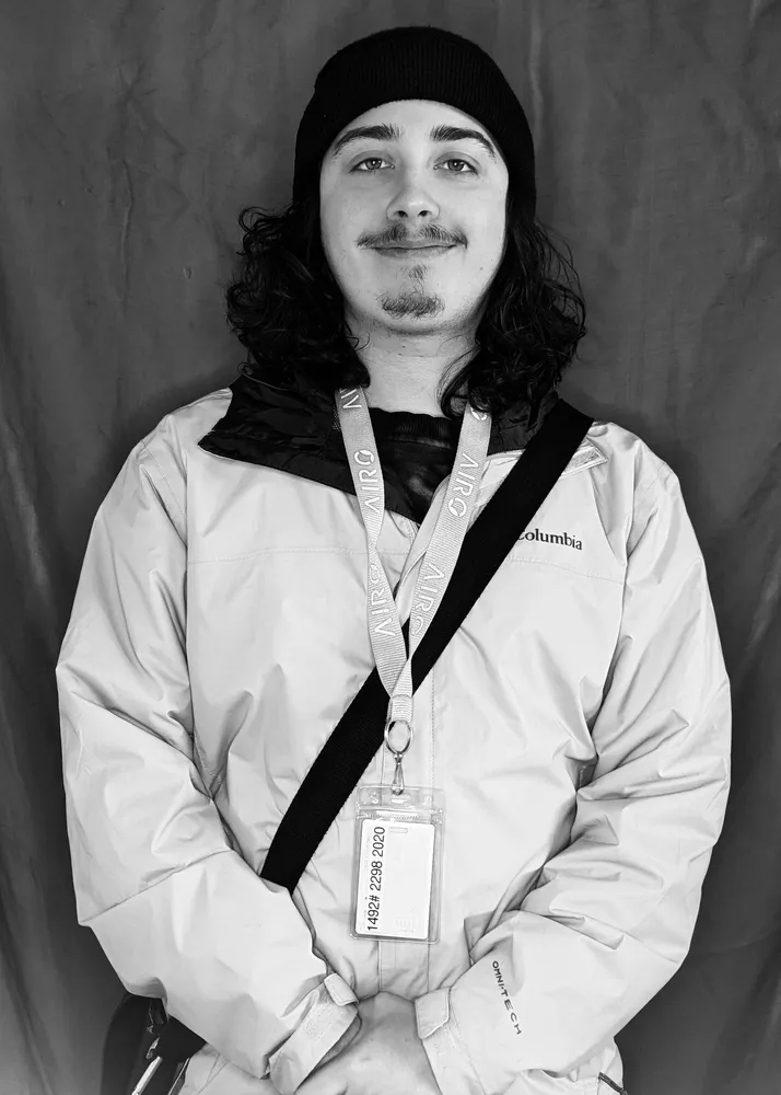Man in winter jacket, beanie, and lanyard, smiling.
