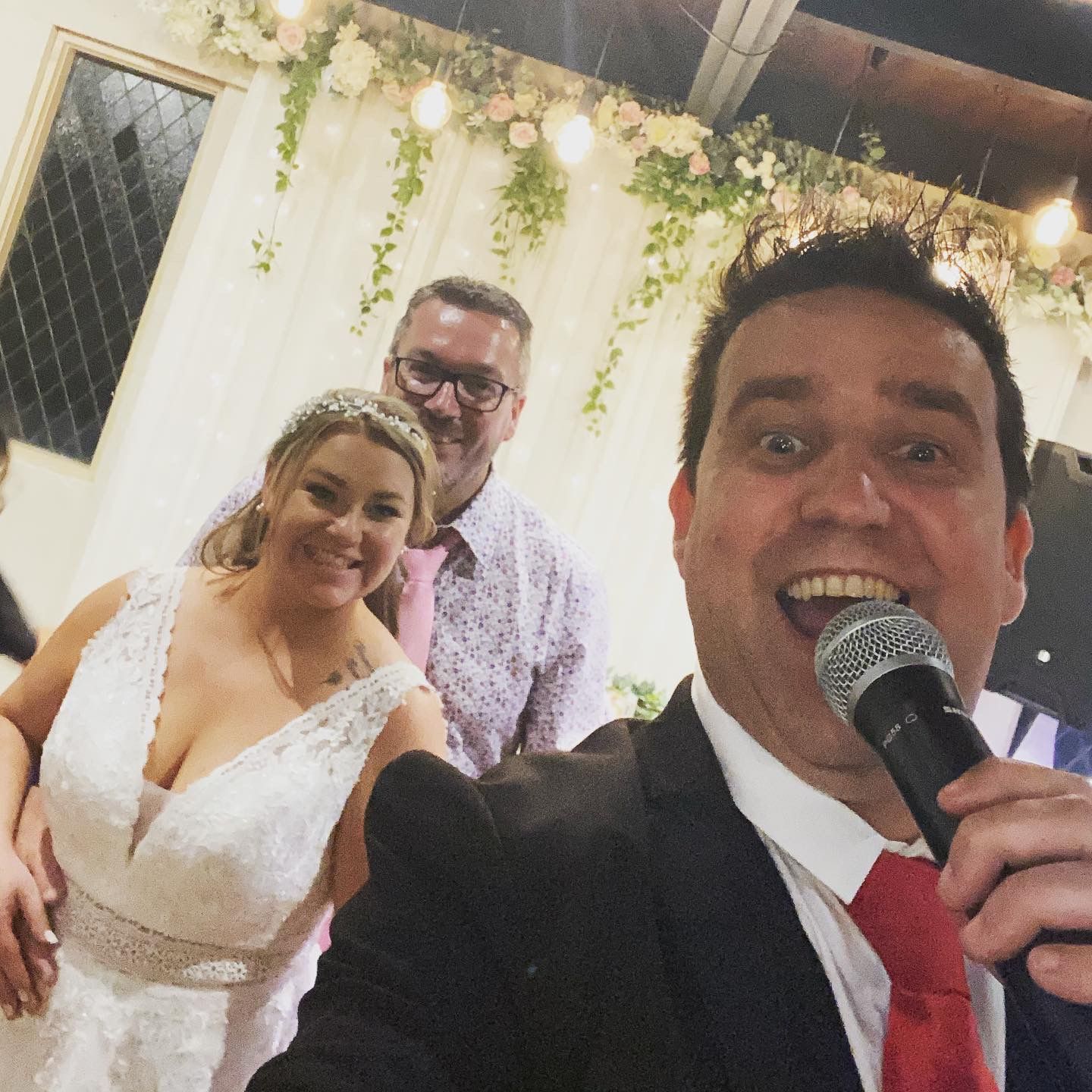 A man is holding a microphone in front of a bride and groom