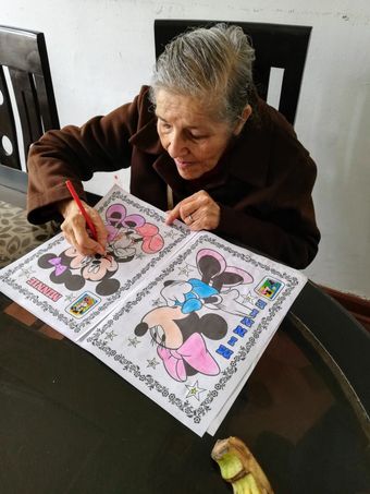 Una mujer colorea una hoja de dibujos animados en una mesa, usando un rotulador rojo sobre una página en blanco y negro.