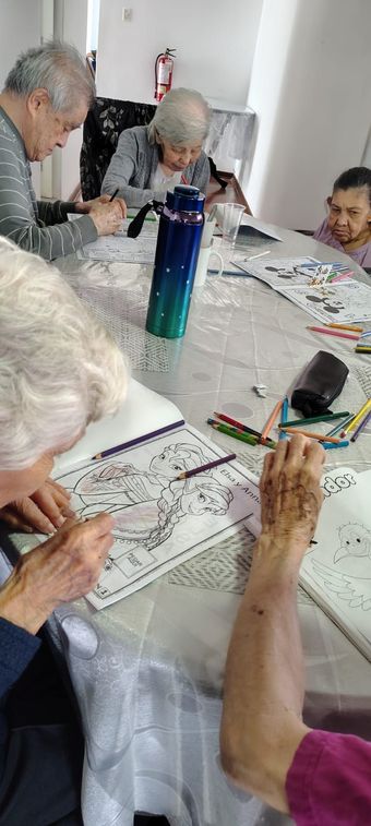 Varias personas sentadas alrededor de una mesa, leyendo y corrigiendo exámenes en una habitación