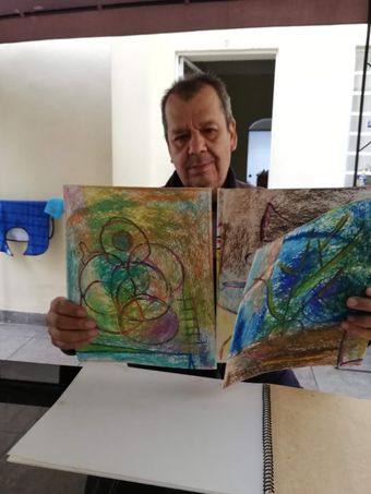 Persona sosteniendo dos coloridos cuadros abstractos en el interior de un edificio.