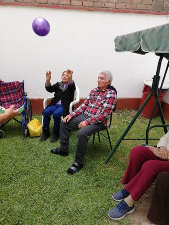 Varias personas sentadas en el césped bajo un toldo, una de ellas lanzando una pelota morada en una reunión 