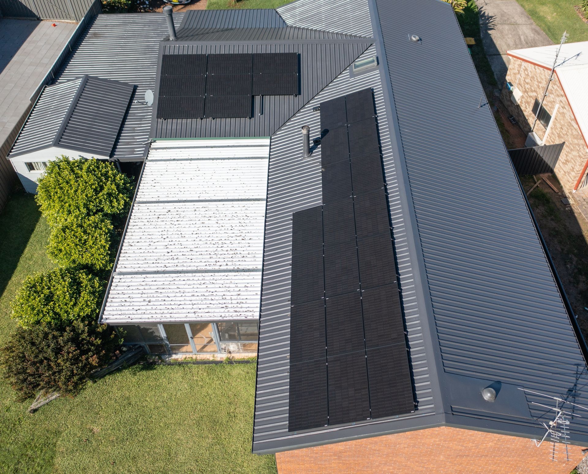 A person installing a solar panel on a gray corrugated metal roof.