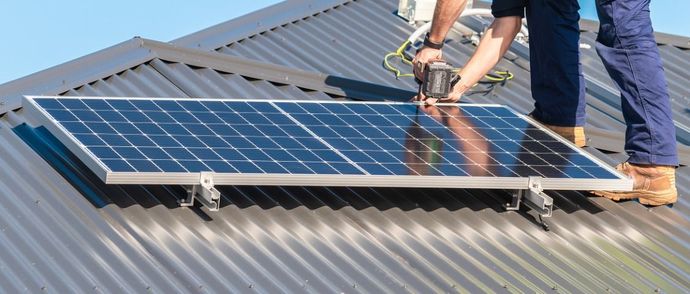 A person installing a solar panel on a gray corrugated metal roof.
