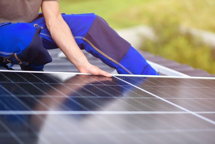 A person installing a solar panel on a gray corrugated metal roof.