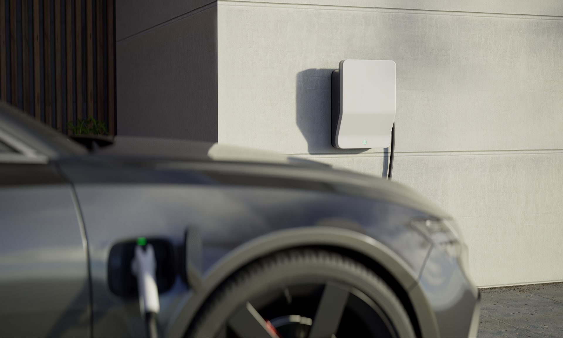 Gray electric car charging next to a white wall-mounted charger, outdoors.